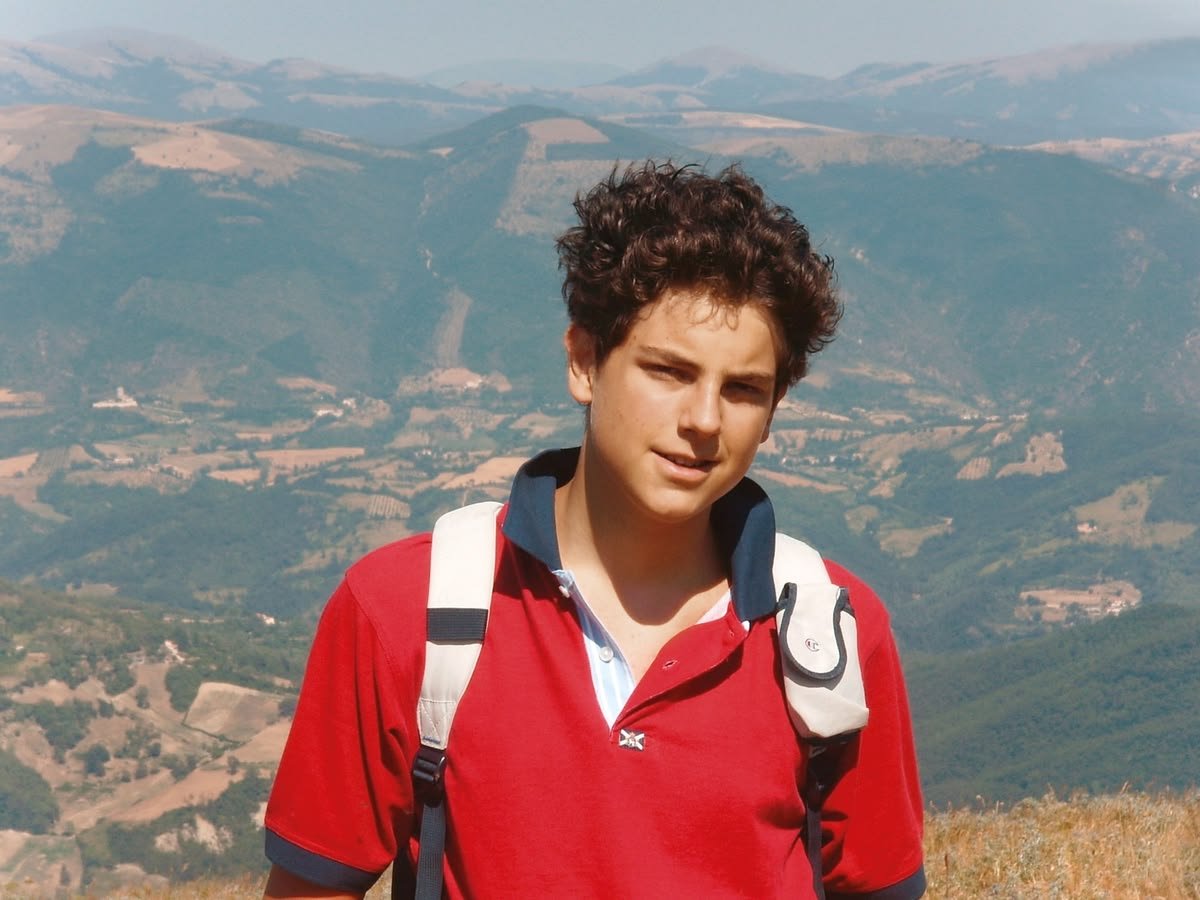 Carlo Acutis en polo rouge, en randonnée