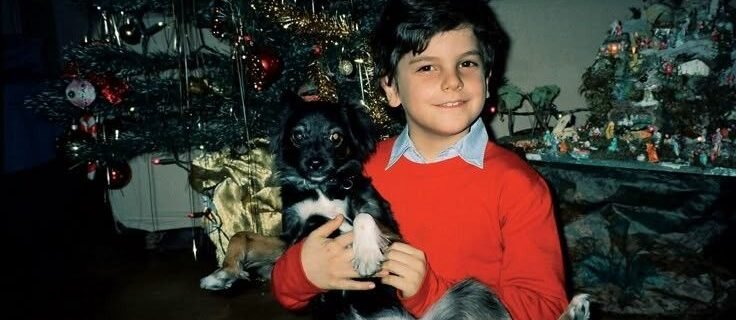 Carlo Acutis enfant, son chien dans les bras, devant le sapin de Noël